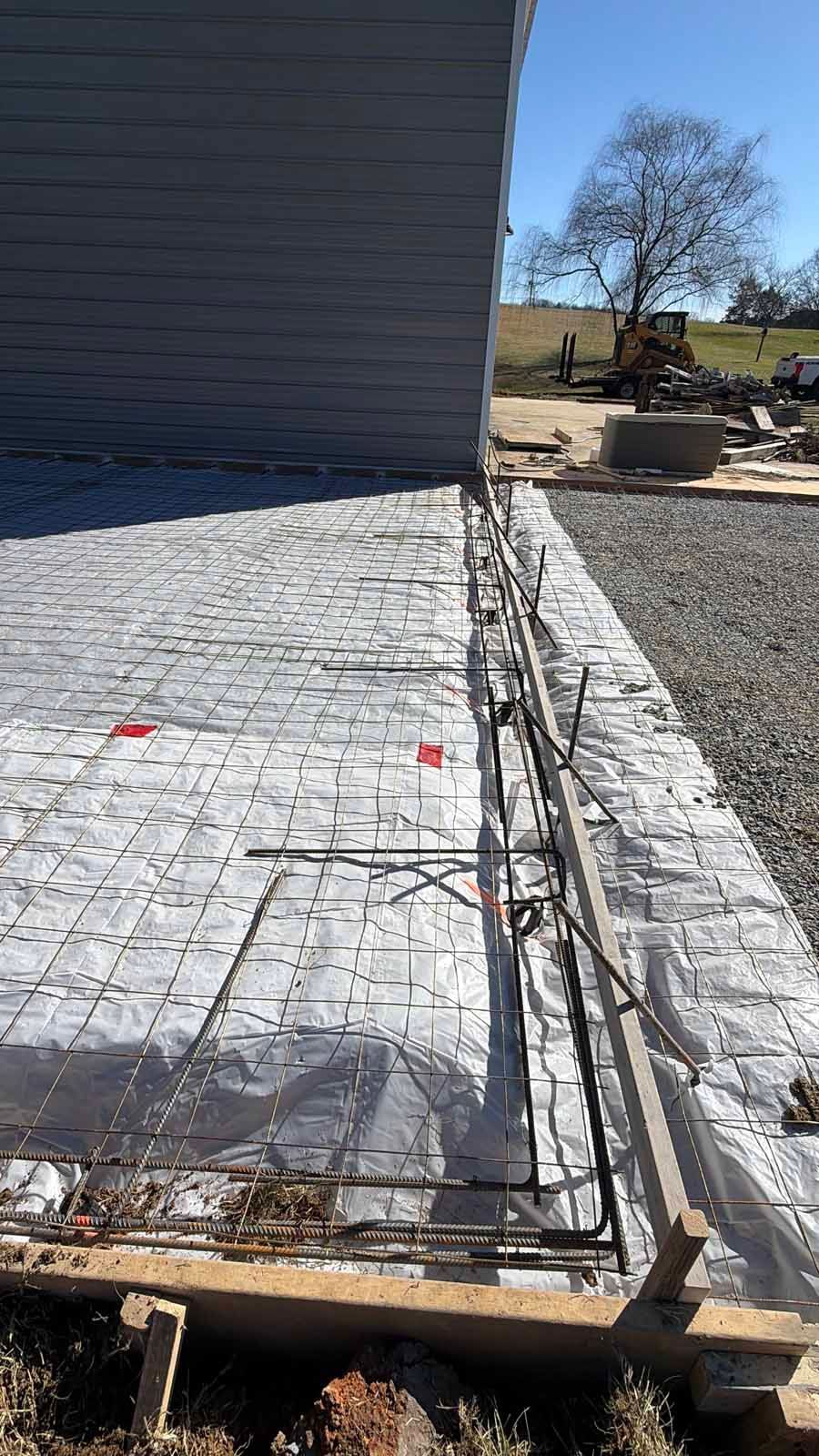 New concrete patio under construction beside a house, with rebar mesh and wooden forms.