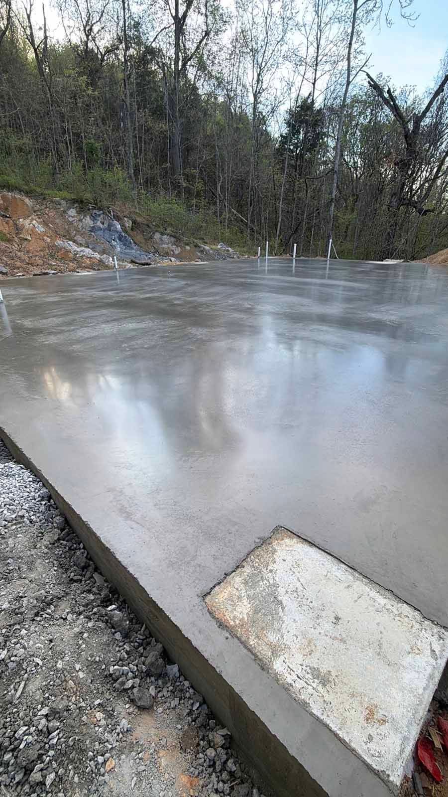 Freshly poured concrete slab beside a wooded area on an overcast day