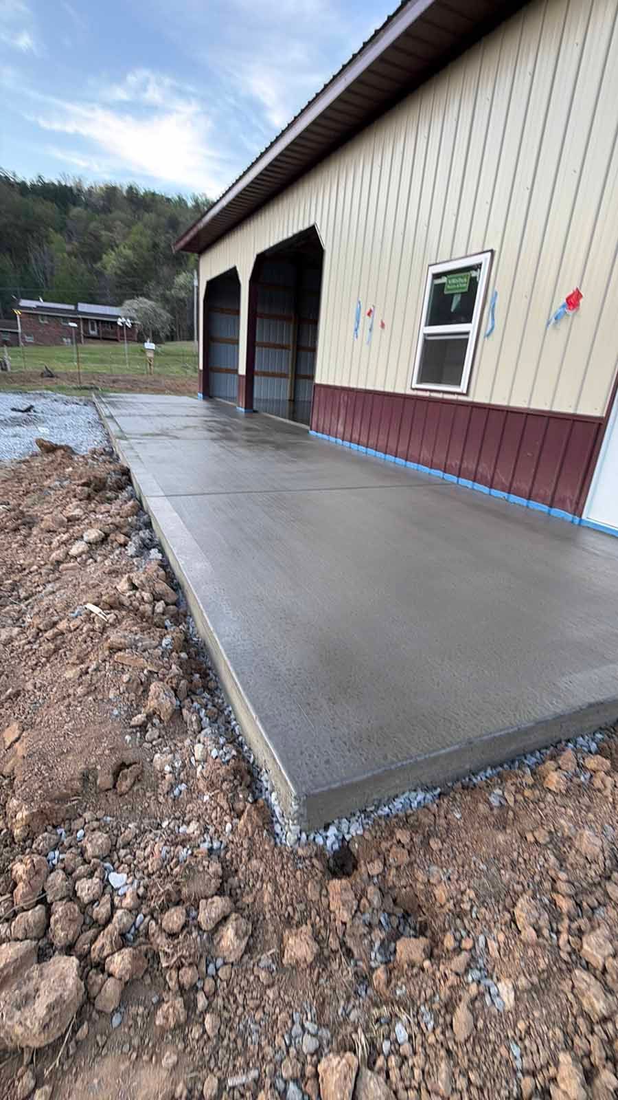 Concrete loading dock beside a tan metal building with a garage bay and muddy gravel foreground