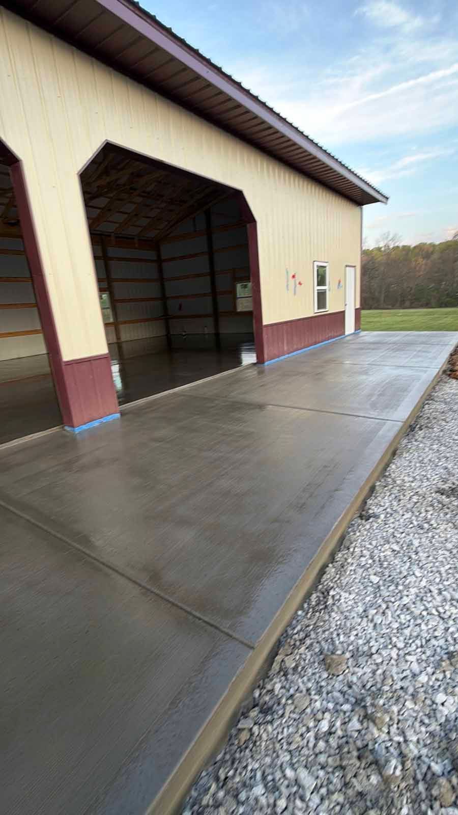 Concrete loading dock beside a tan metal building with open bay door and gravel driveway