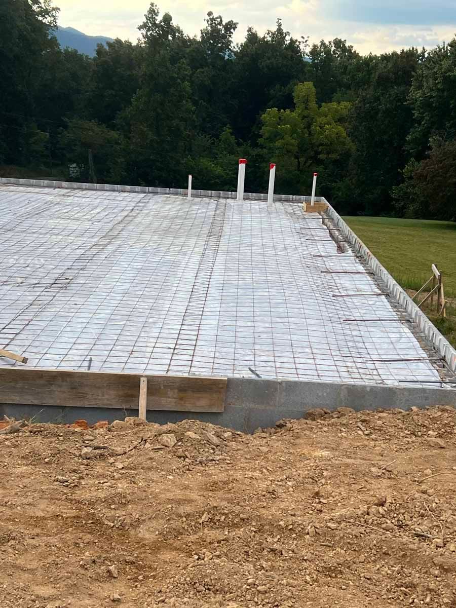 Insulated foundation slab under construction with white vapor barrier and plumbing pipes, wooded background