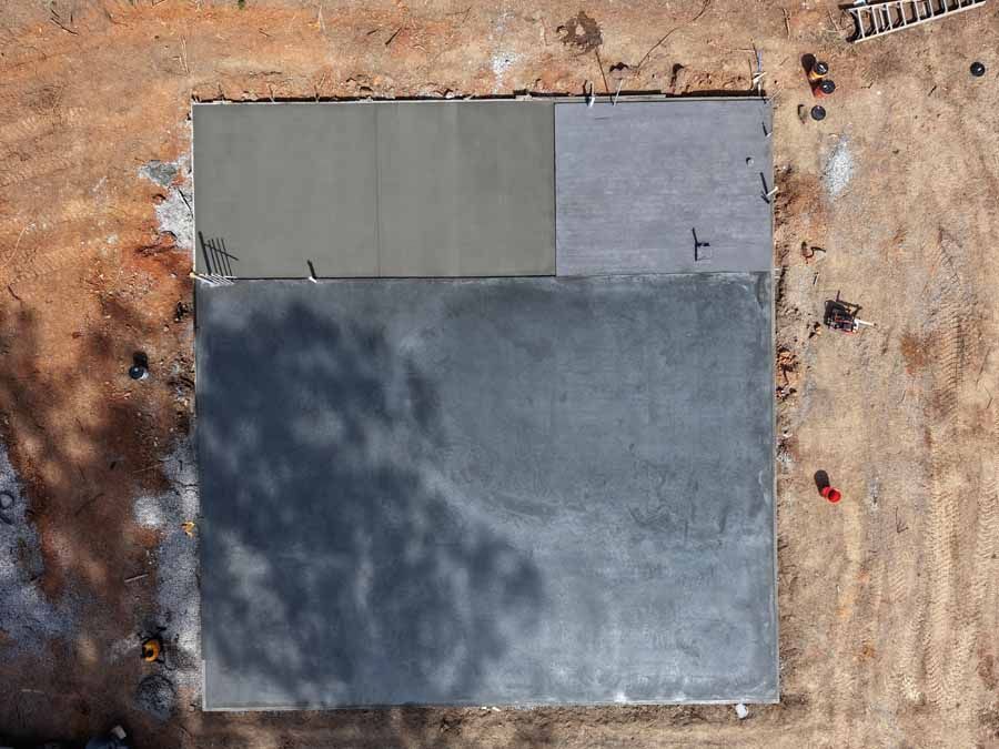Aerial view of a small concrete slab with two lighter sections on a dirt construction site.