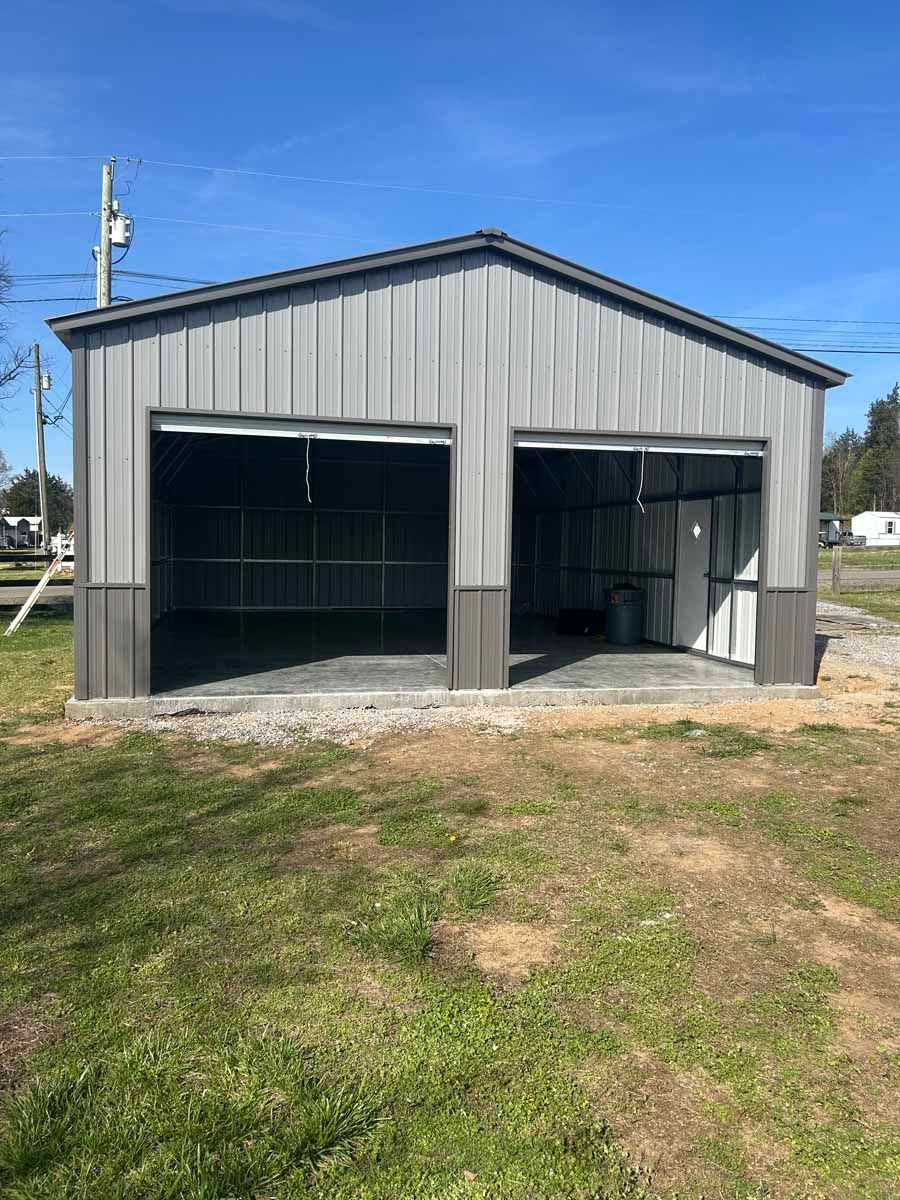 Gray metal barn with two open bays on a grassy lot under a blue sky