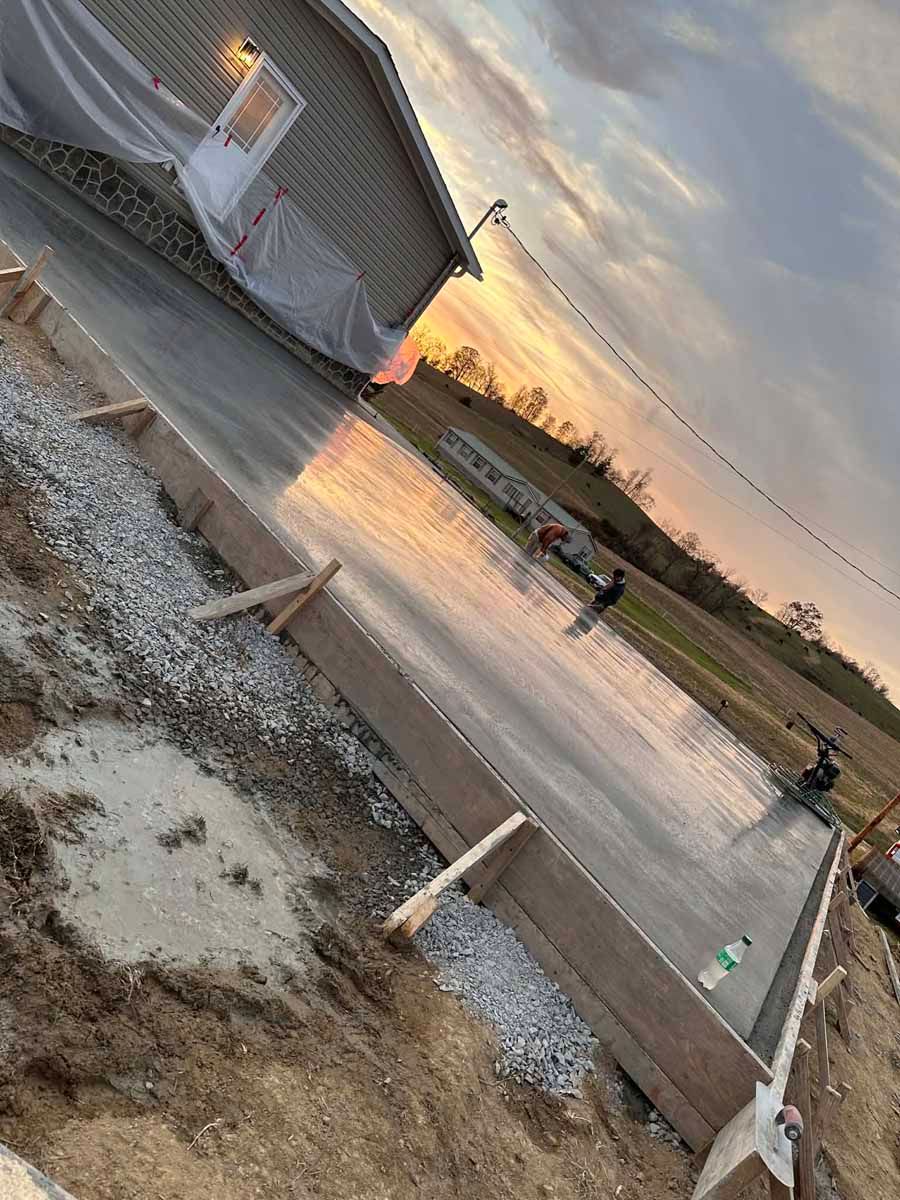 Snow-dusted roadside at sunset with a small building, cones, and a person walking along the wet pavement