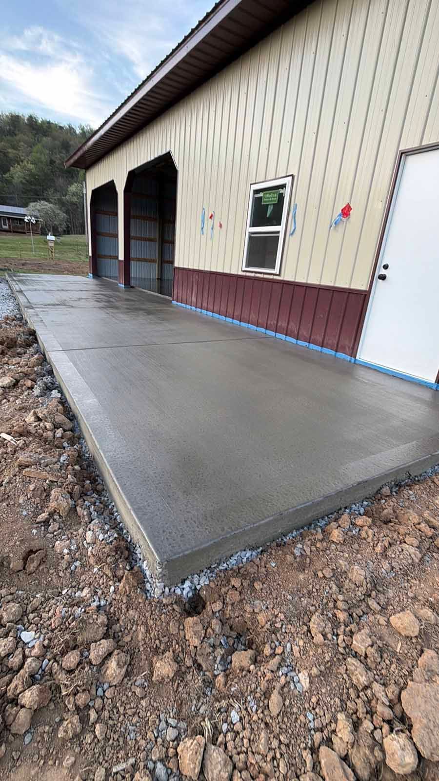 Fresh concrete slab beside an industrial building with garage doors and a white side door