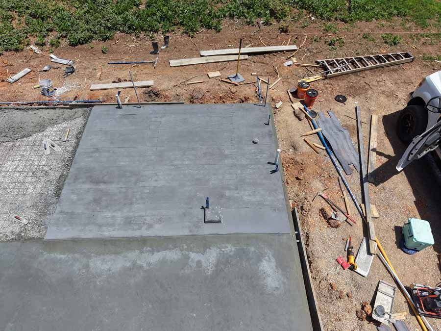 Roof under construction with wet gray concrete slab, tools, and lumber scattered around the site