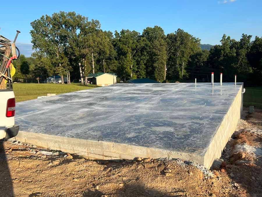 Fresh concrete foundation slab at a construction site with trees and blue sky in the background