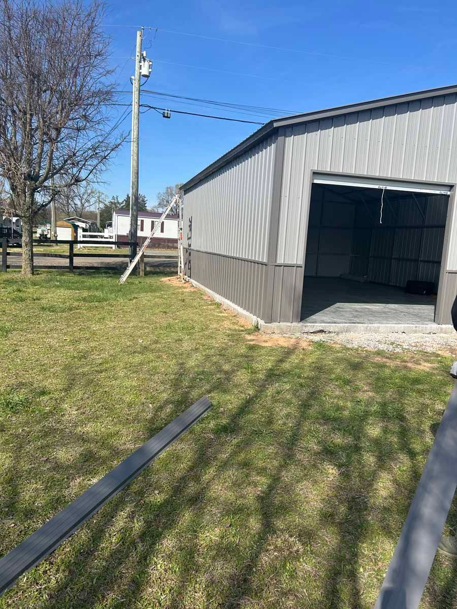 Metal shed with open garage door beside a grassy yard and utility pole, with shadows across the ground