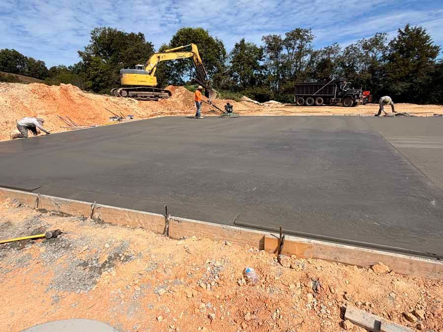Construction site with an excavator smoothing fresh asphalt on a large paved area under a blue sky