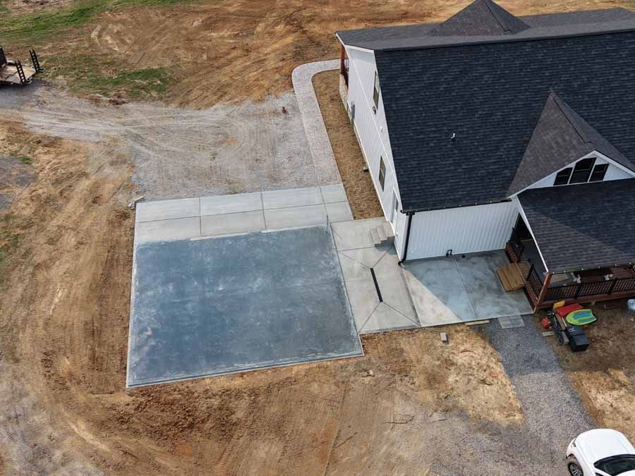 Aerial view of a house with a new concrete driveway or patio beside it.