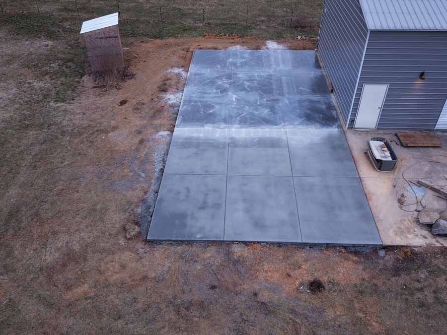 Backyard patio with newly laid gray concrete pavers beside a gray house and bare dirt yard