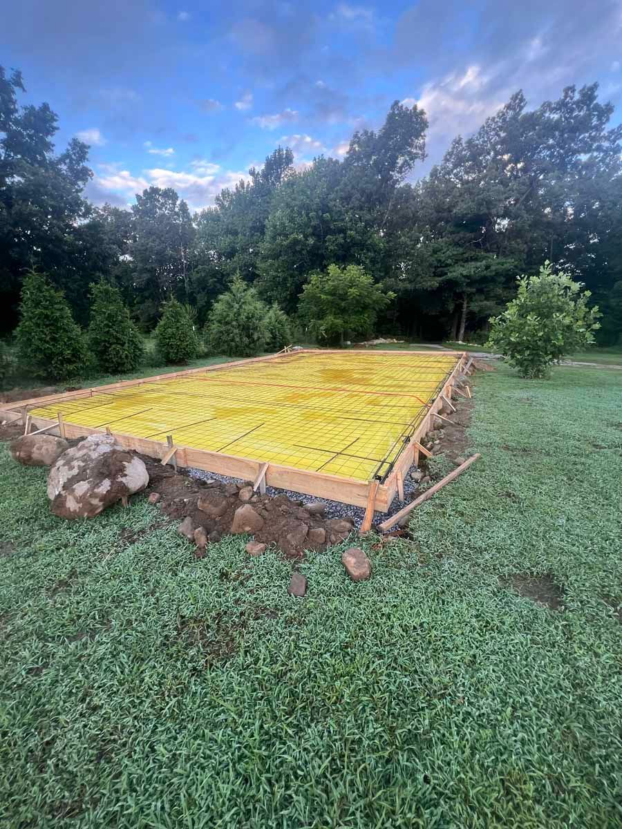 Raised garden bed with bright yellow cover in a grassy yard, bordered by trees under a cloudy sky