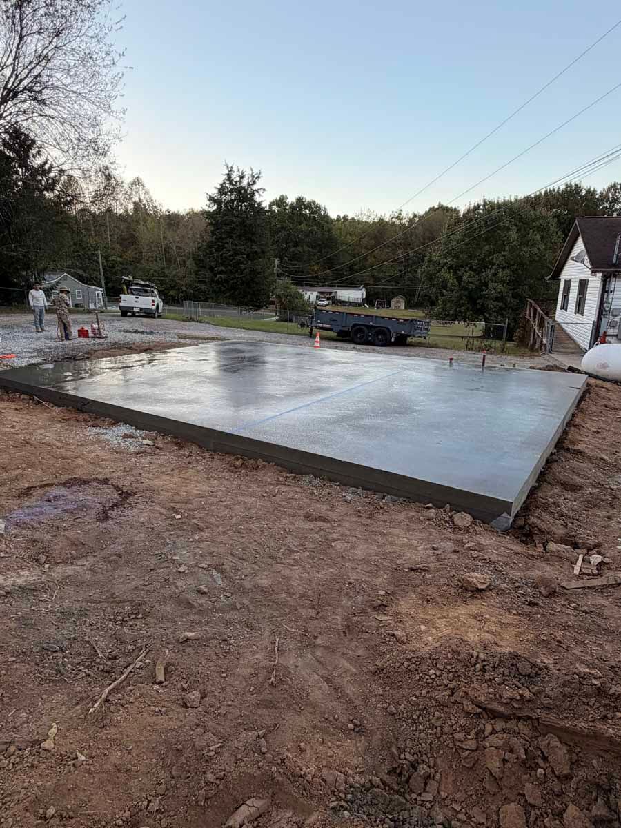 Freshly poured concrete slab at a residential construction site with dirt foreground and trees around