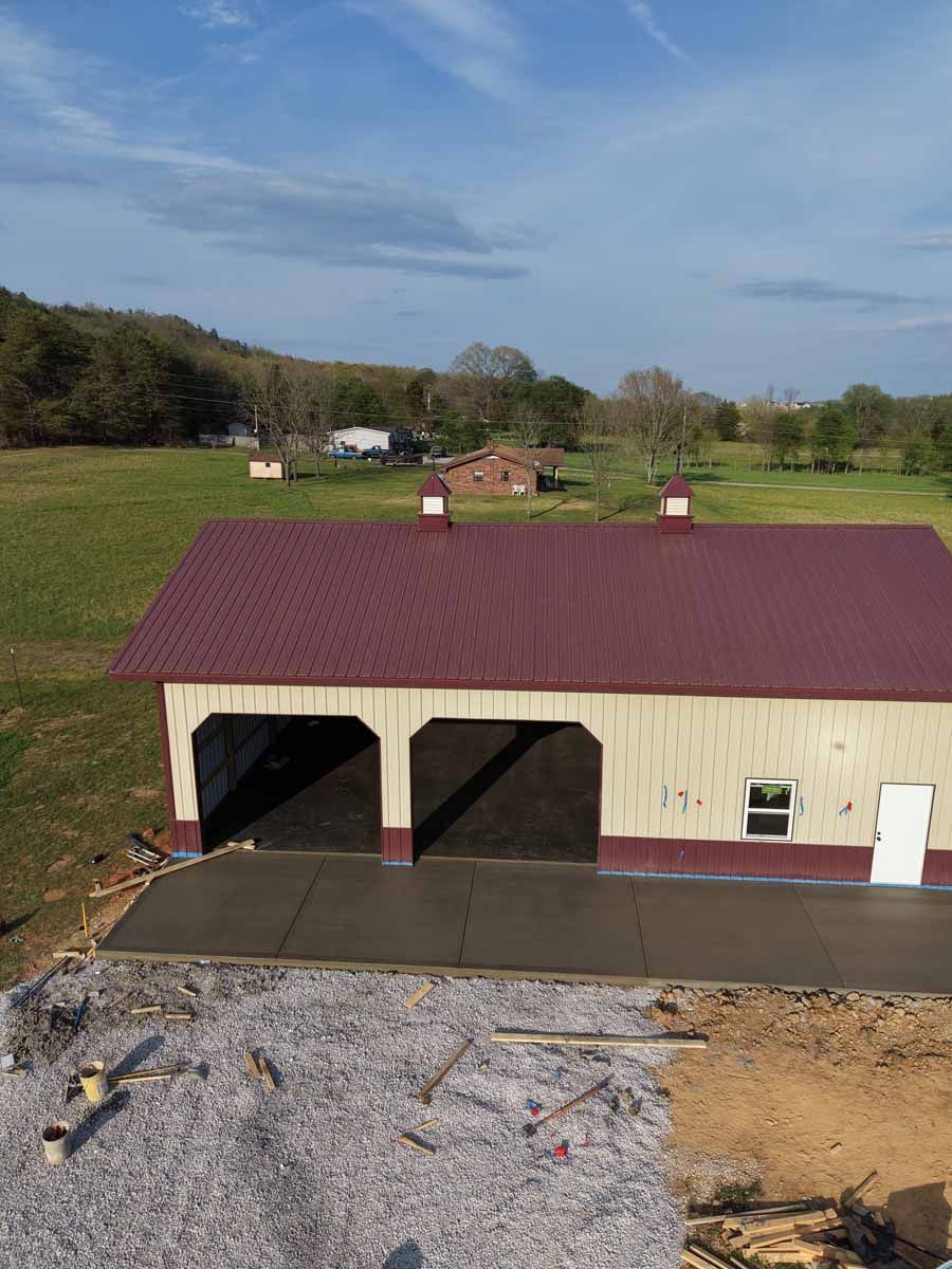 Red-roofed barn with open bays on a rural hillside under a blue sky