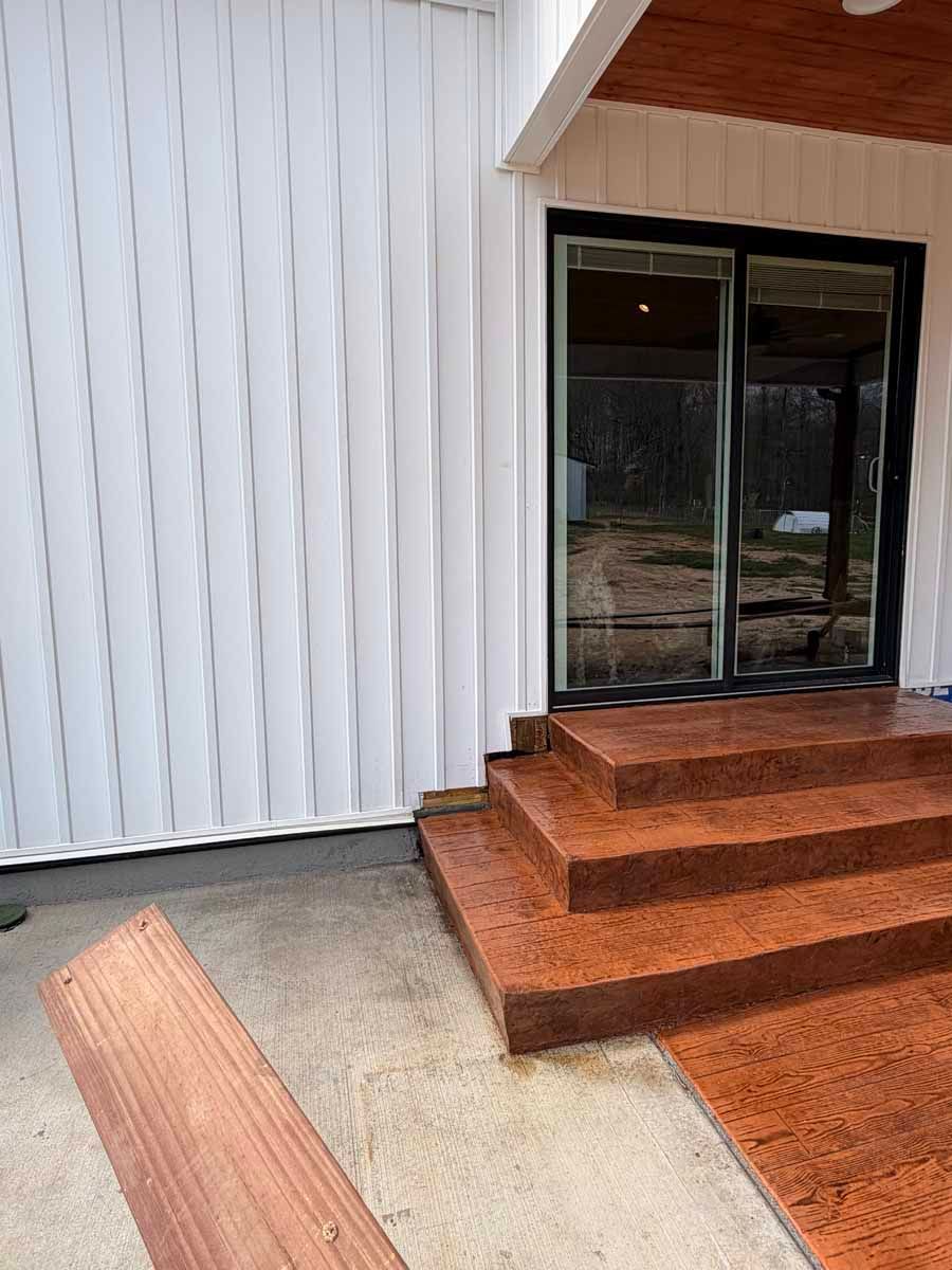 Sliding glass door beside rust-colored steps on a white-paneled building exterior