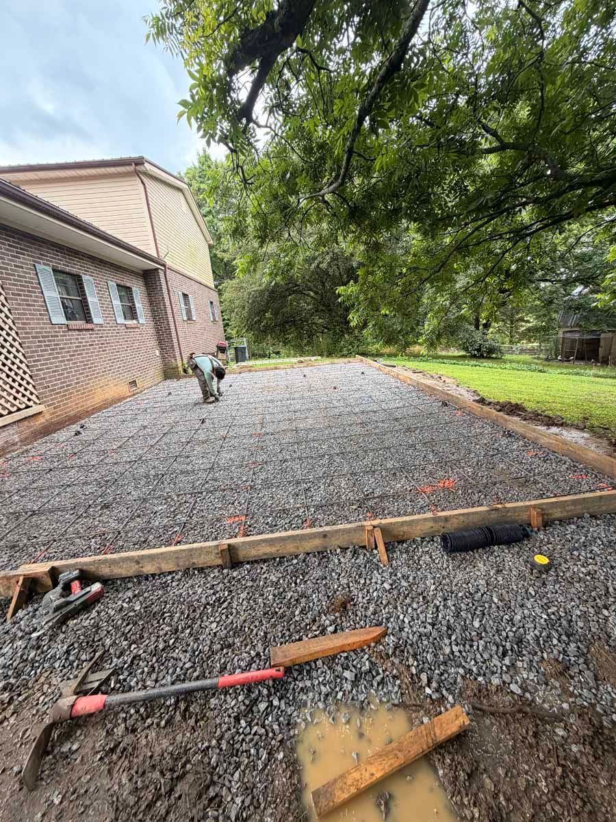 Gravel path beside a brick house, with tools and lumber in the foreground and trees lining the yard