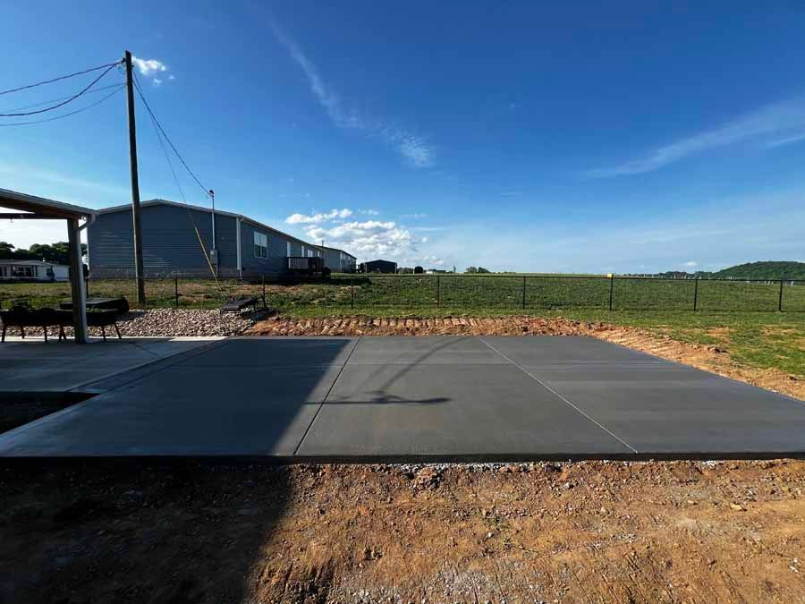 Concrete pad beside a rural building and field under a blue sky