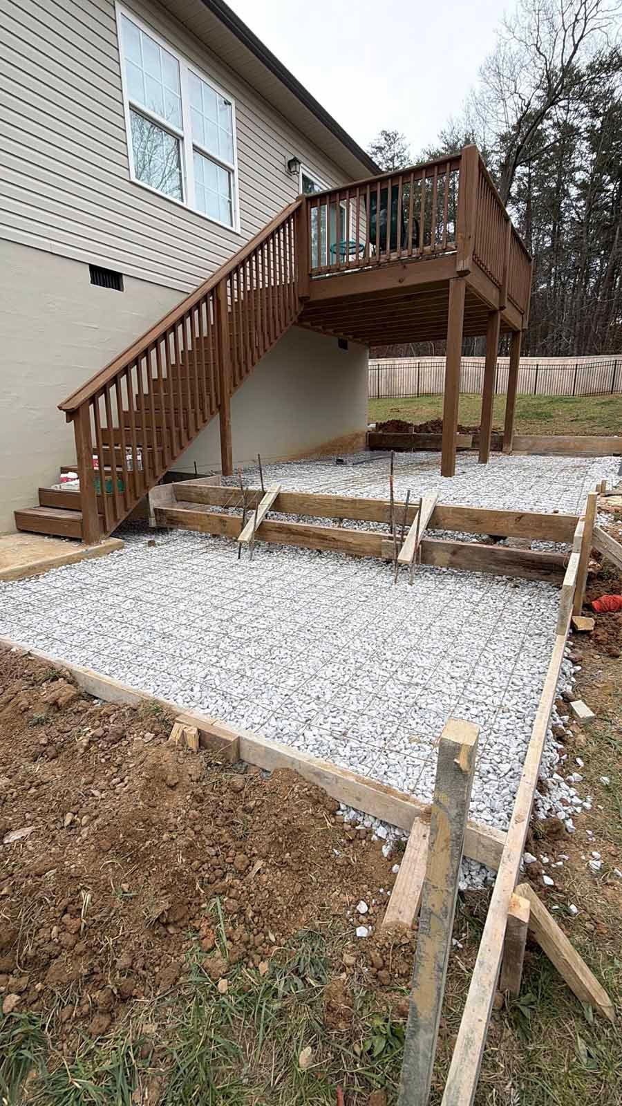 Backyard wooden deck with stairs beside a house, overlooking a gravel-covered patio area