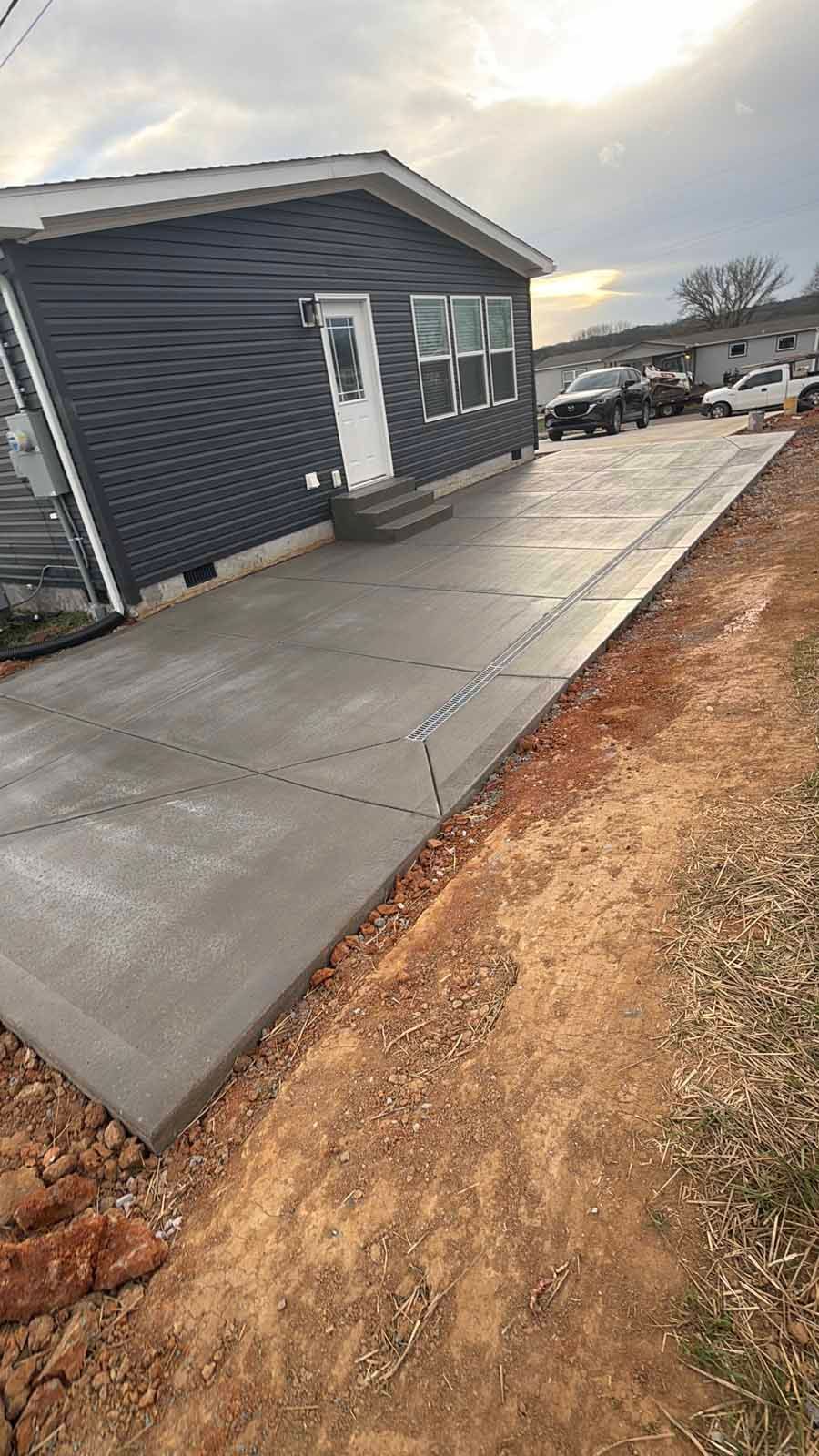 Concrete sidewalk beside a dark gray building, with muddy ground and a cloudy sky.