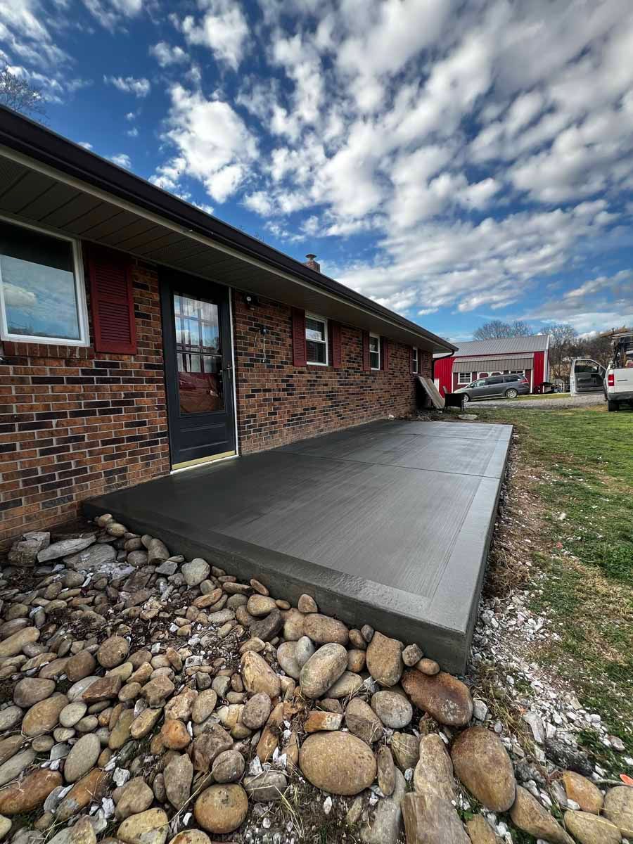 Concrete patio beside brick house with stone border and cloudy sky overhead