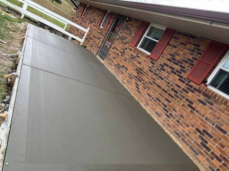 Tilted view of a brick house with red shutters and a smooth gray concrete driveway or ramp
