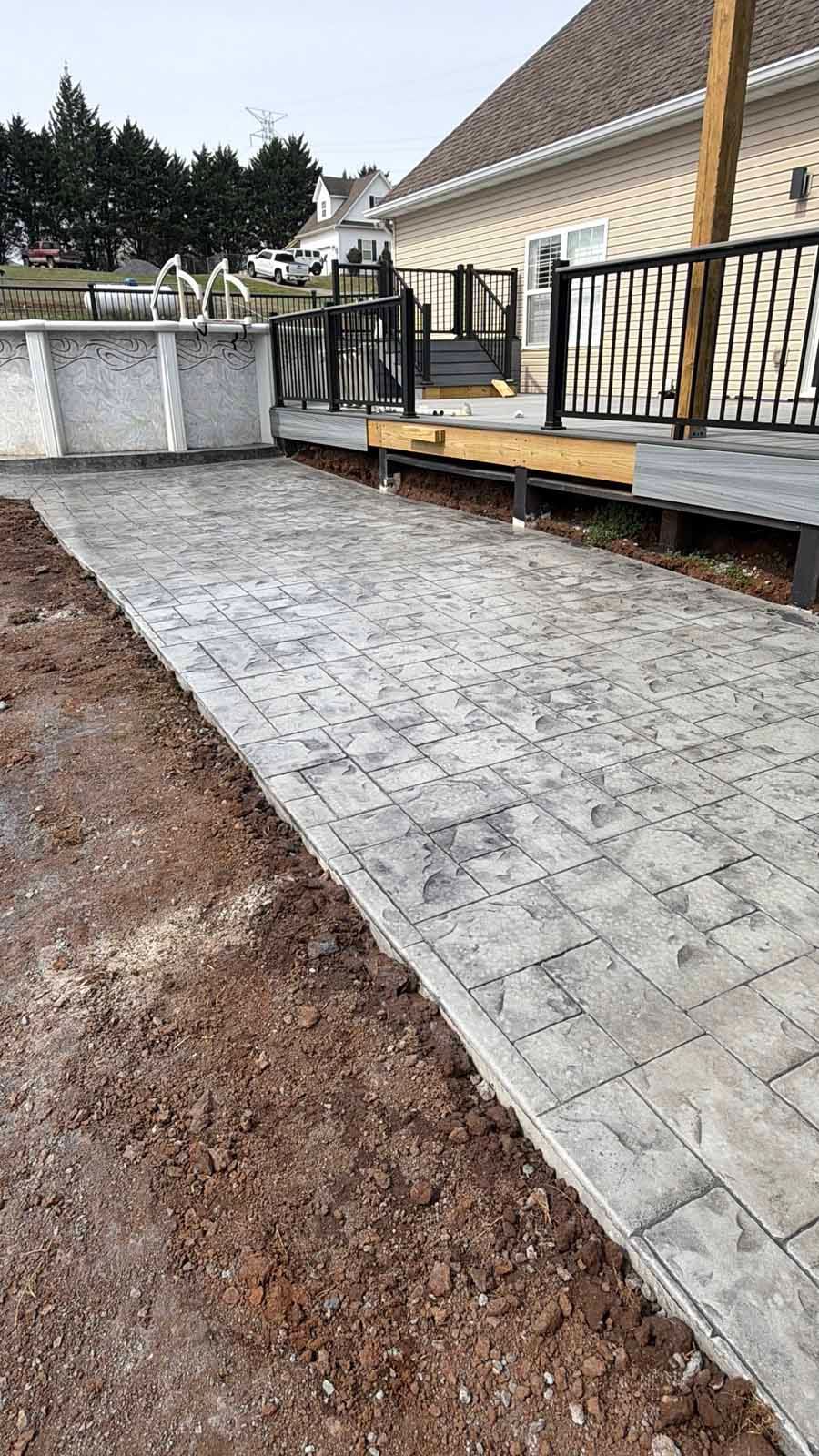 Partially completed gray paver walkway beside a house, with black railing and gravel soil edge