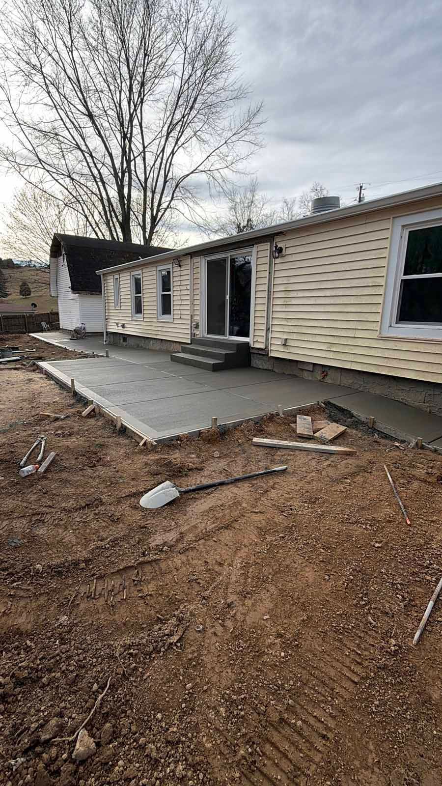 Partially renovated beige house with a new concrete porch and bare yard under a cloudy sky