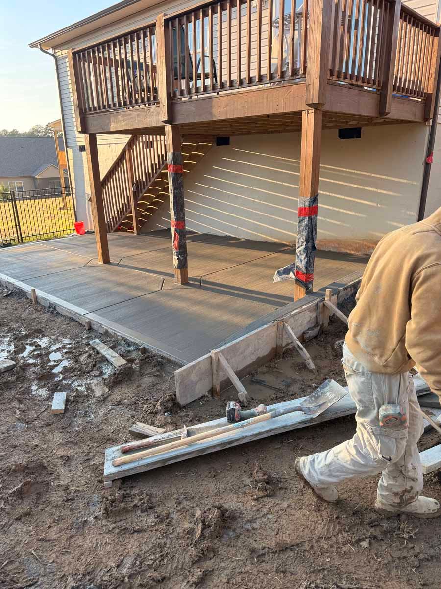 Deck under construction beside a concrete slab, with a worker and tools in the foreground.