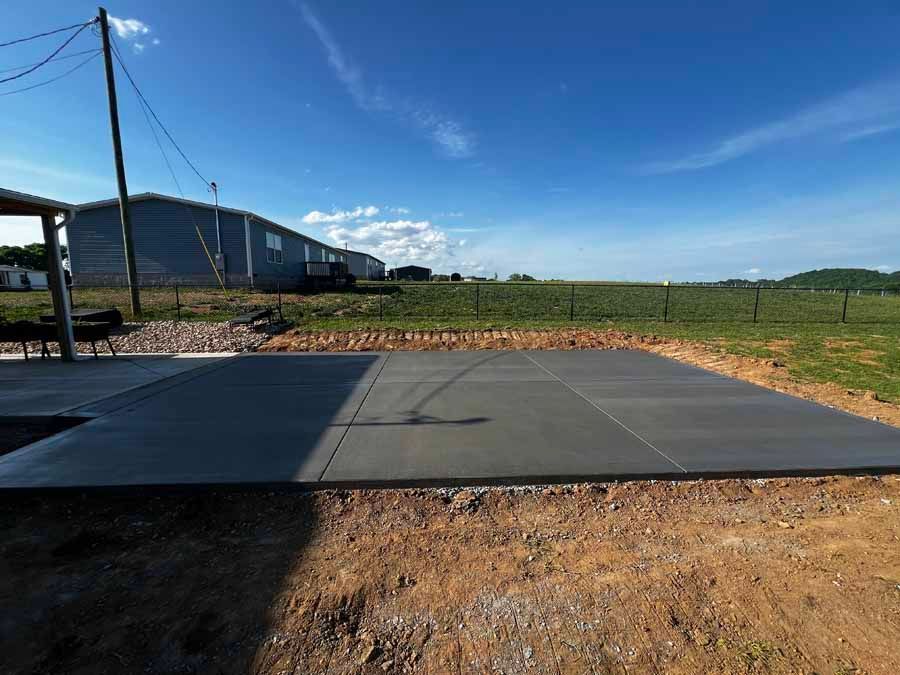 Outdoor concrete pad beside a rural building under a blue sky, with gravel, grass, and utility poles nearby