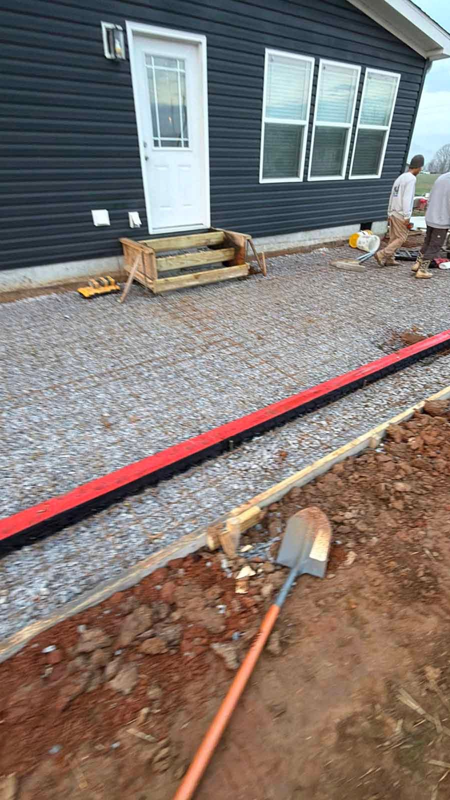 Gravel yard beside a dark house with workers installing edging and a red hose in the foreground