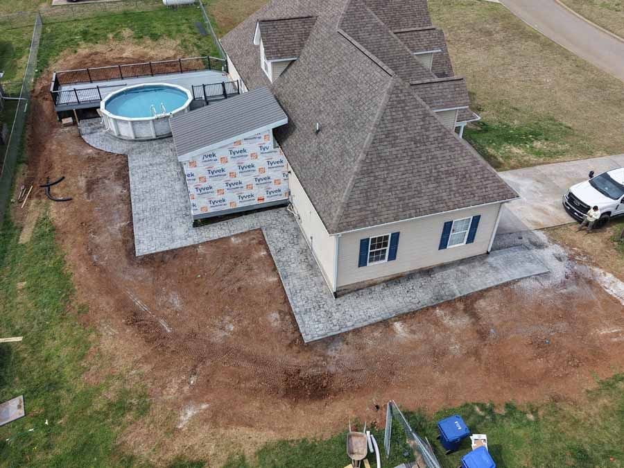 Aerial view of a house with a small pool, patio, and dirt yard in a rural setting
