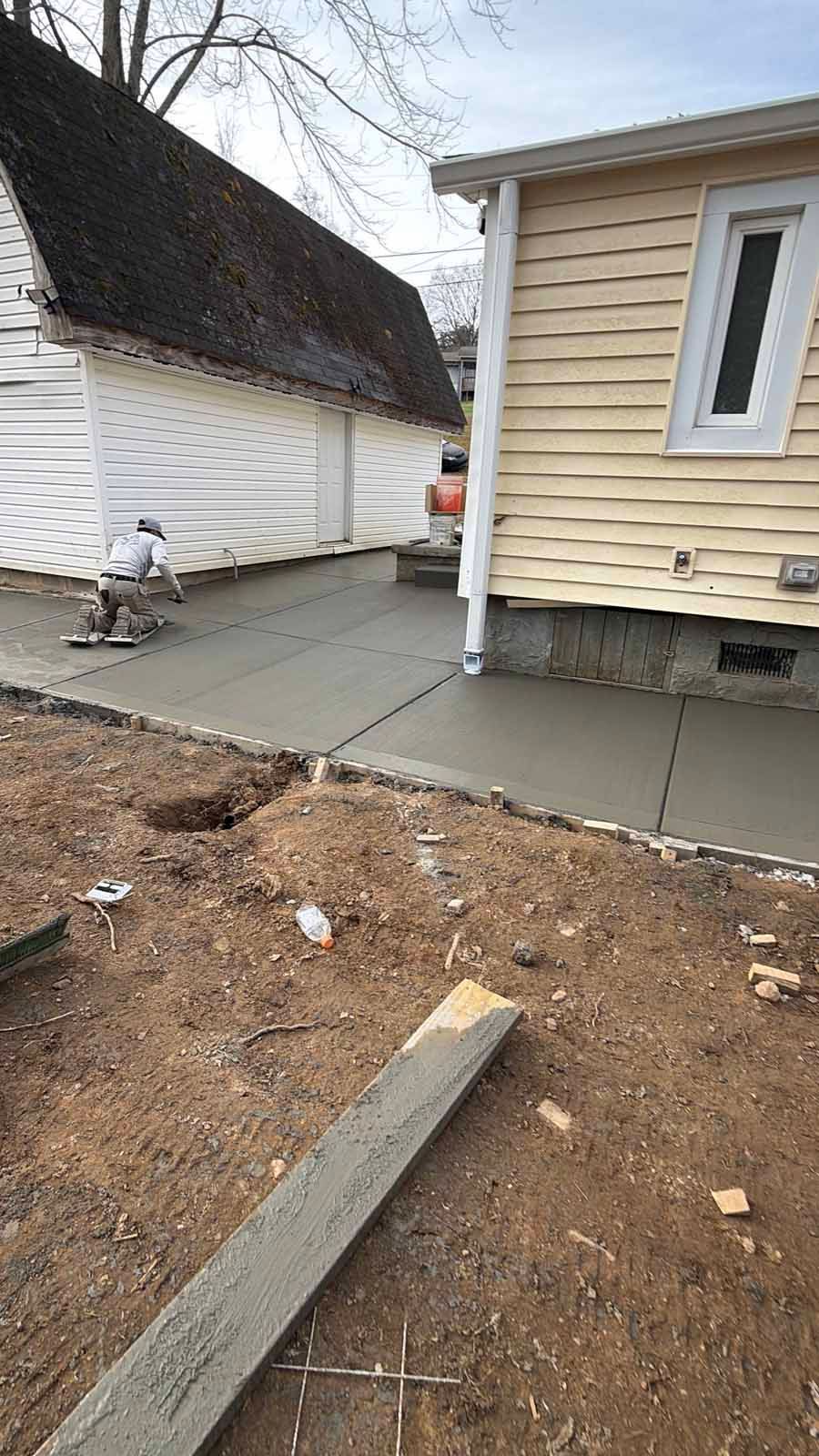 Backyard patio beside a beige house, with concrete slabs and bare dirt in the foreground.