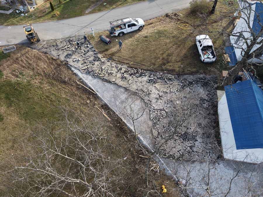 Overhead view of a rocky roadside slope with two parked white vehicles near a blue-roofed building.