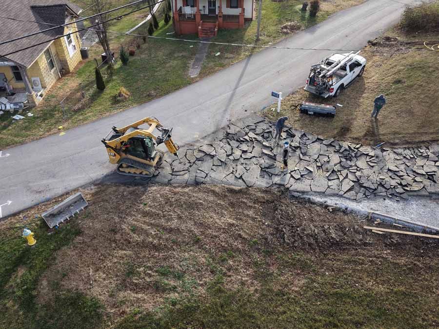 Bulldozer and white utility truck at a damaged roadside embankment with broken concrete slabs.