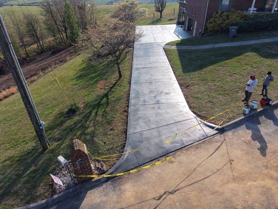 Concrete ramp on a grassy slope with two people walking beside it near a building.