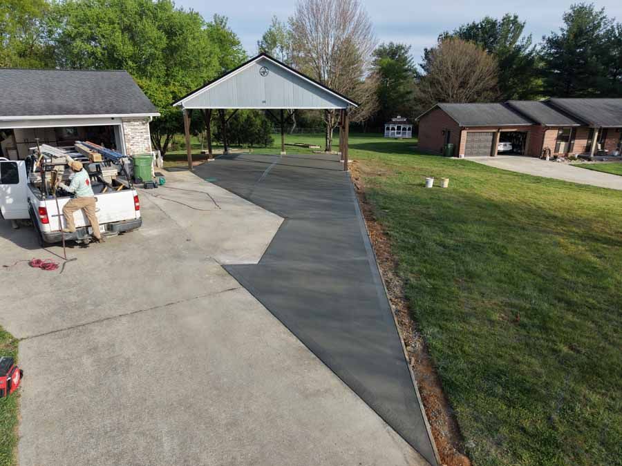 Concrete driveway with a dark resurfaced strip leading to a carport beside a house and yard