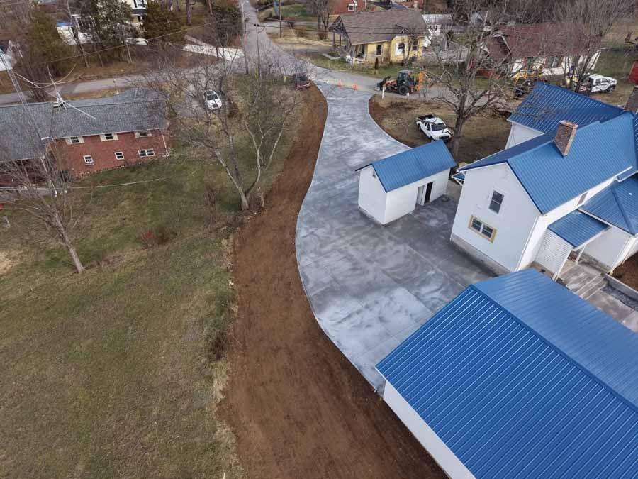 Aerial view of a rural property with blue-roofed buildings, driveway, and a muddy path beside grassy land
