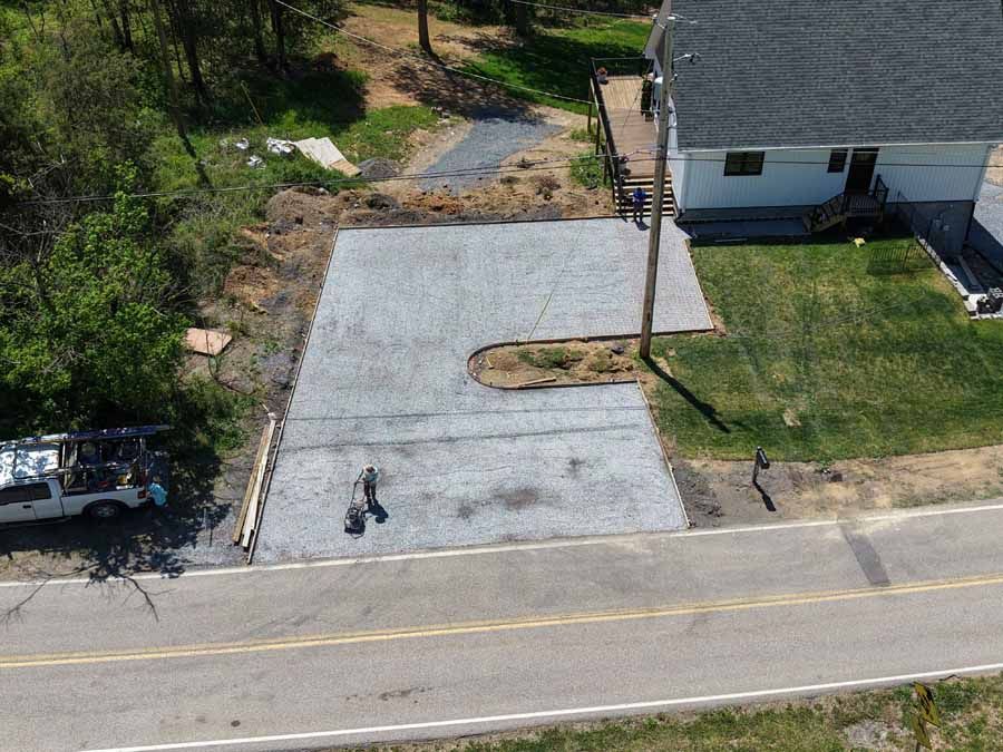 Aerial view of a new concrete driveway beside a road and house, with a small landscaped island.