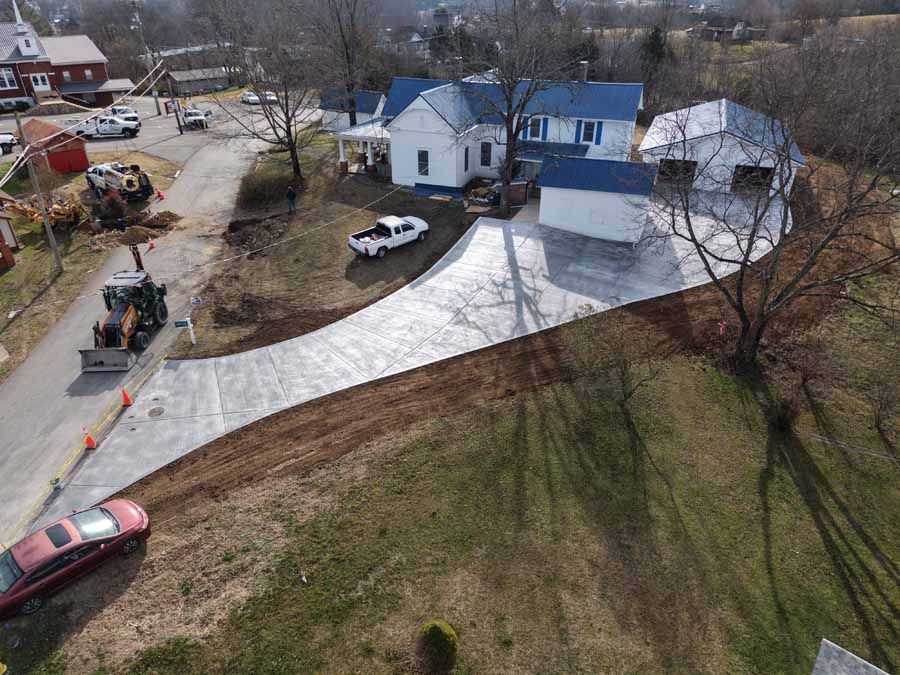 Aerial view of a snowy suburban street with houses, parked cars, and a driveway coated in white plastic.