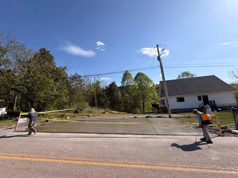Two workers crossing a road with yellow caution tape near a house and utility pole on a sunny day
