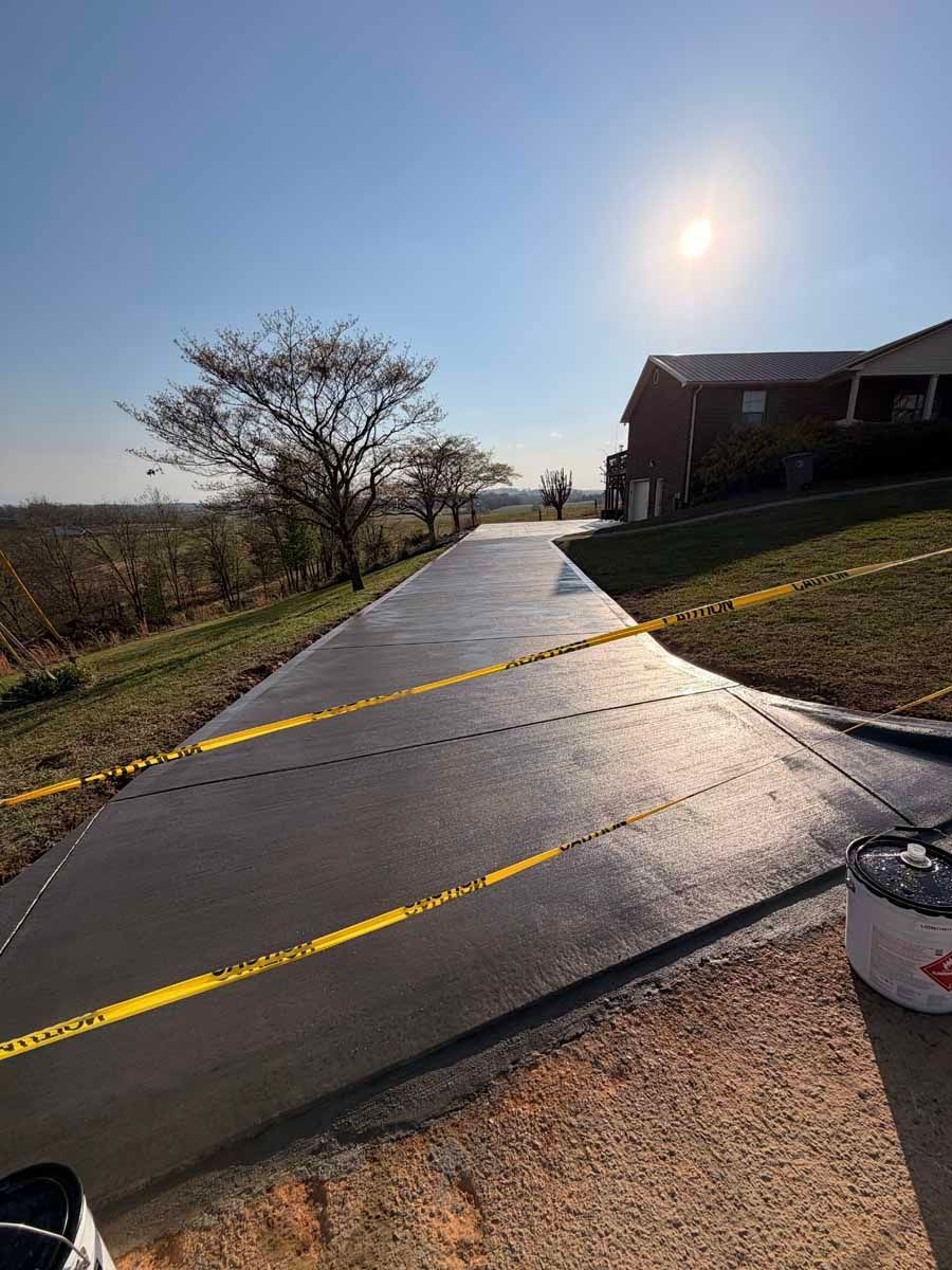 Sunny paved path blocked by yellow caution tape beside a house and trees