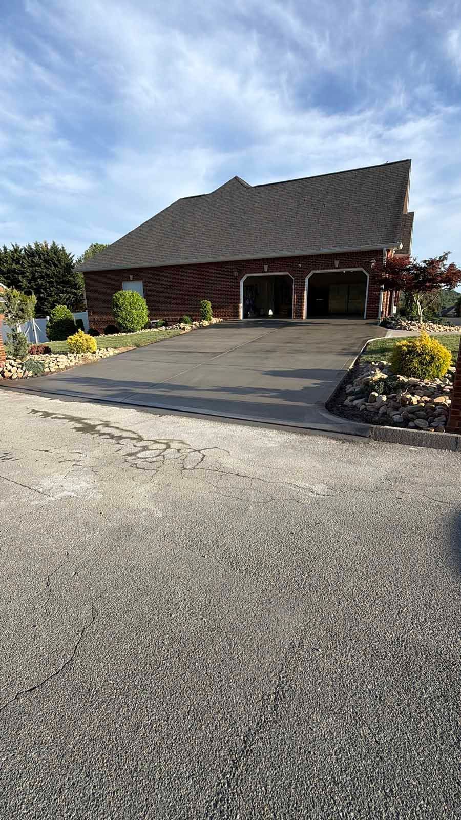 Brick building with a steep roof and dark driveway, surrounded by flower beds under a clear sky
