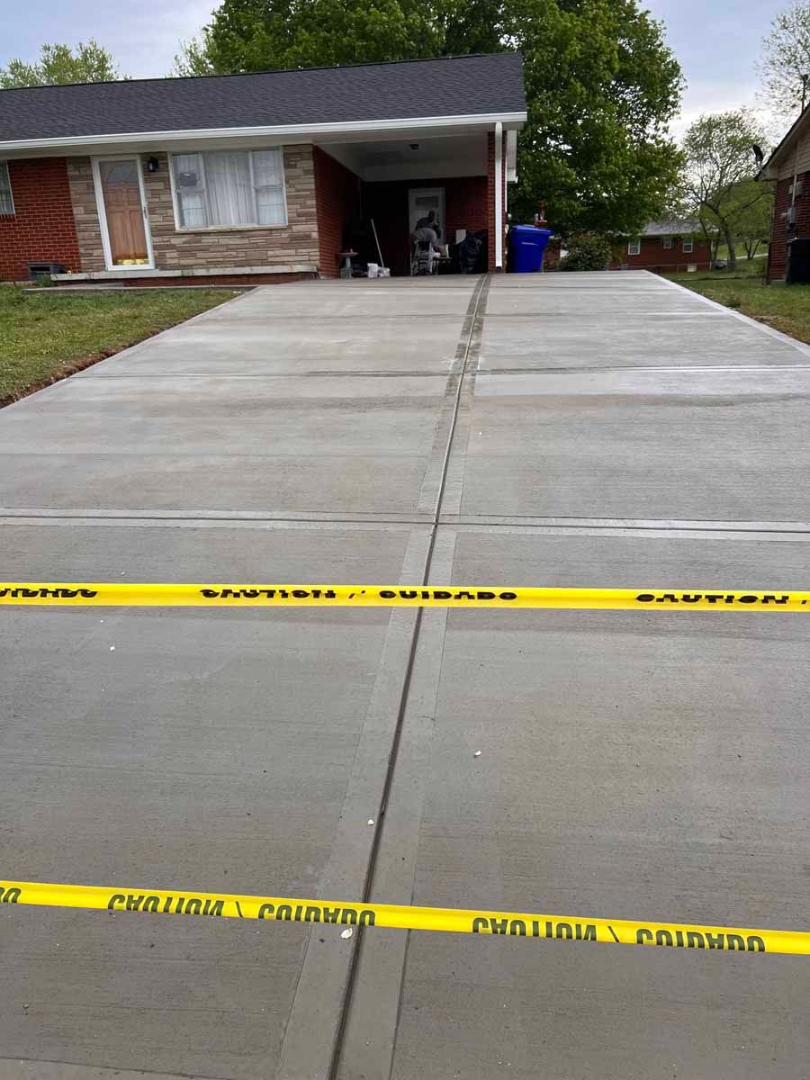 Fresh concrete driveway with yellow caution tape in front of a brick house
