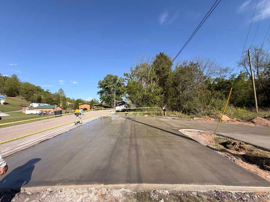 Freshly paved road under construction on a sunny suburban street with trees and utility lines