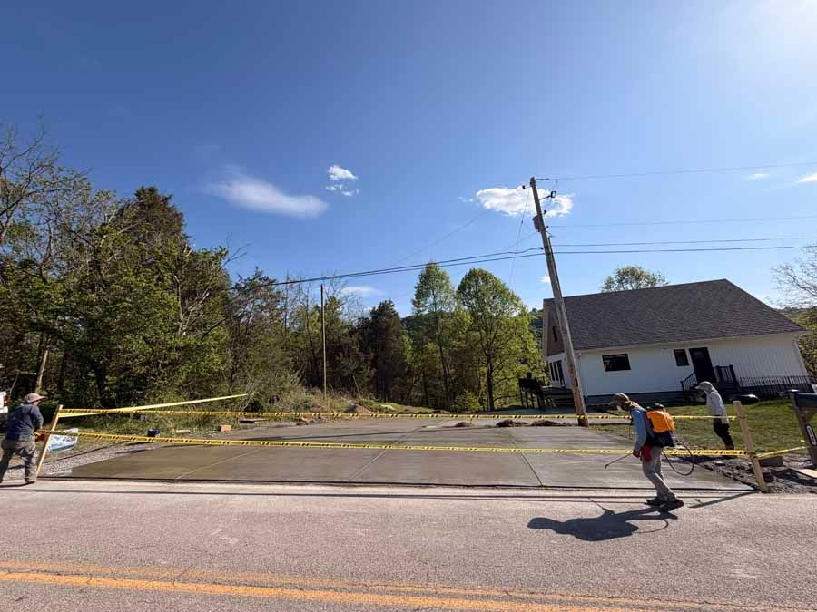 Yellow caution tape blocks a damaged road as workers inspect storm debris near a house.