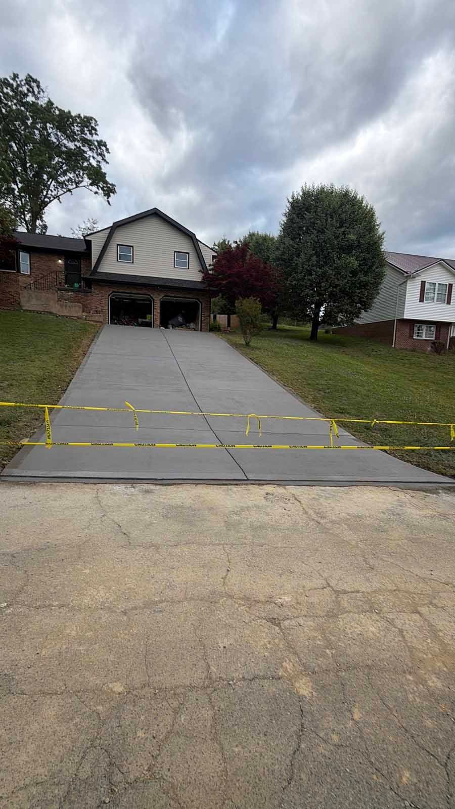 Steep driveway leading to a house with an open garage, trees, and cloudy sky