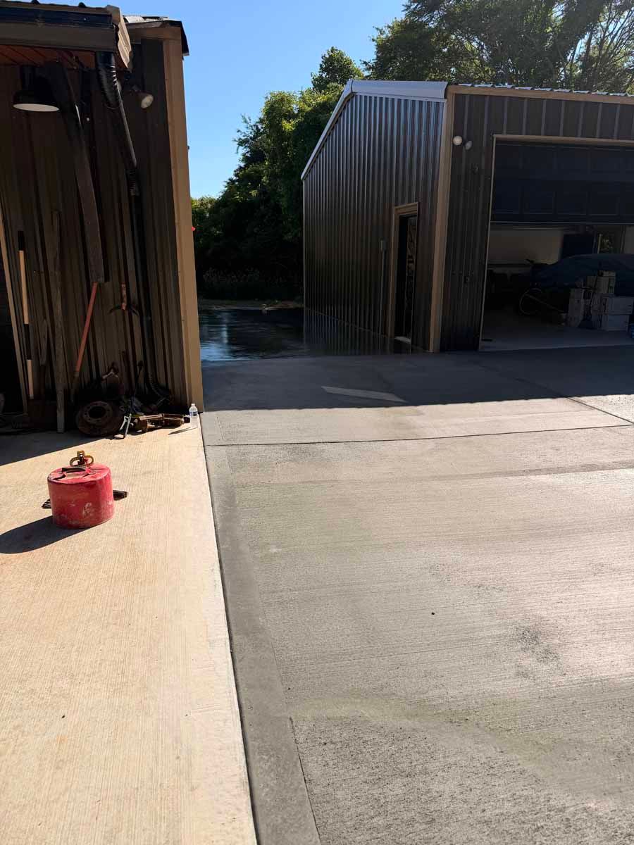 Outdoor industrial yard with open metal sheds, a concrete driveway, and a red fuel can in the foreground