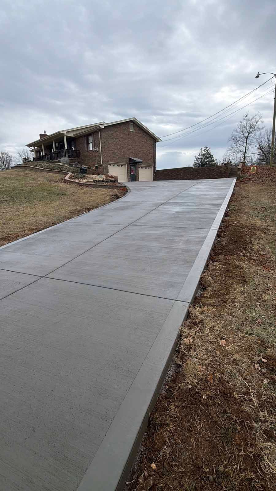 Concrete driveway leading up to a brick house on a cloudy day