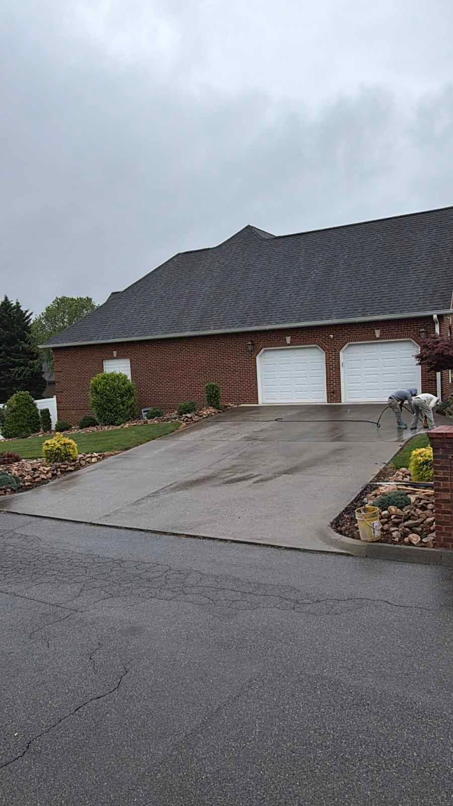 Brick house with two white garage doors and a sloped driveway under a cloudy sky