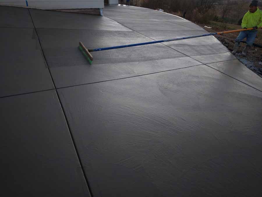 Worker smoothing freshly poured concrete with a long broom on a sloped driveway